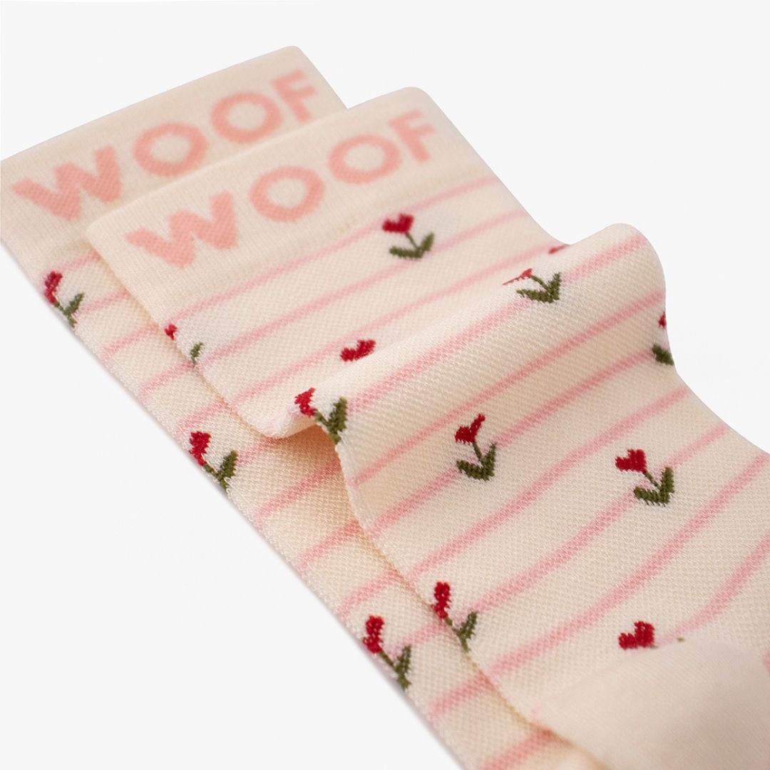 Macro close-up shot showing the Sweet Buds Bamboo Crew Compression Socks folded neatly to highlight the pink woven "WOOF" cuff bands and the striped tulip bud knit pattern layout.